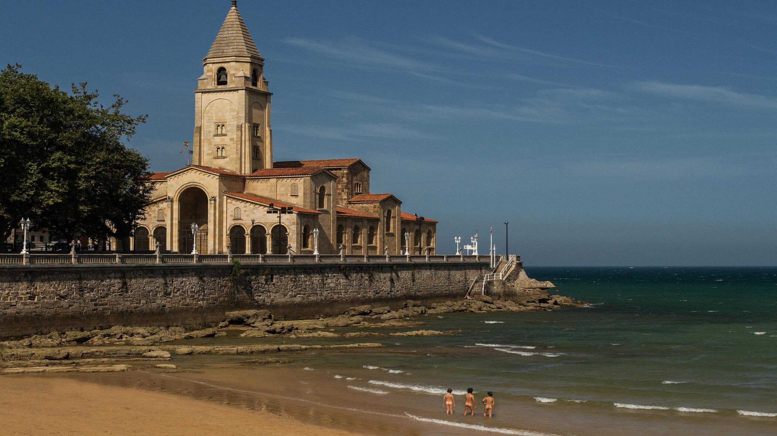 Charming coastal church next to a beach with people in the sea.